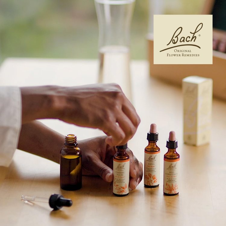 Un gros plan d'une main en train d'appliquer un compte-gouttes sur une bouteille d'extraits floraux de Bach, avec d'autres flacons en arrière-plan.