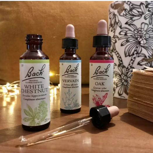 Trois flacons de fleurs de Bach sur une table en bois, avec des étiquettes indiquant 'White Chestnut', 'Vervain' et 'Oak'.