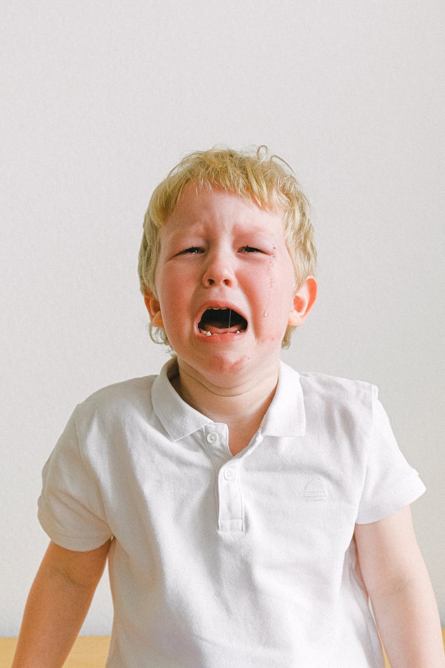 Un enfant blond en polo blanc pleure, montrant des larmes sur son visage.